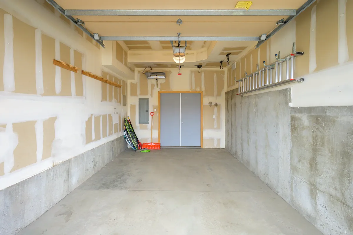A clean, spacious garage with storage shelves, ladders, and an uncluttered concrete floor. The area is ideal for securely storing bikes, skis, sleds, and other outdoor equipment.