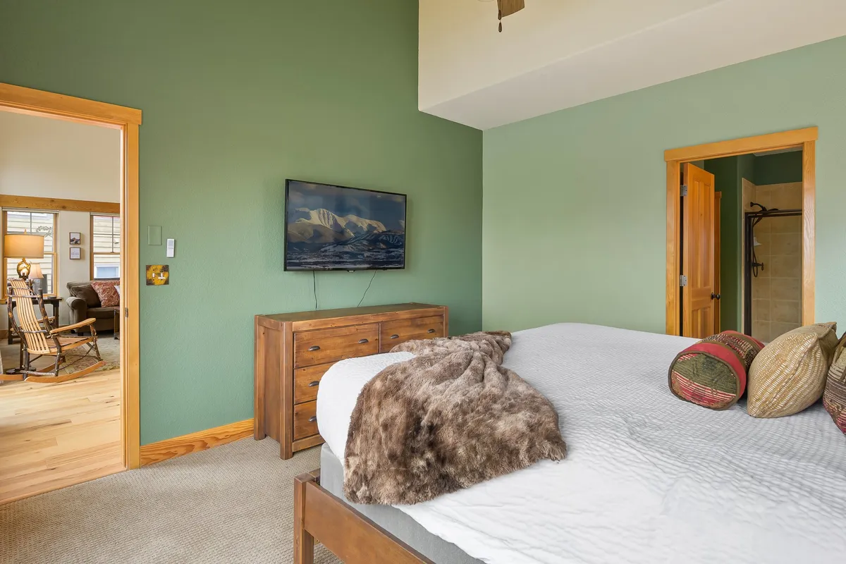 A bedroom scene with a bed adorned with decorative pillows and a cozy throw, a dresser with a TV, and a doorway leading to another room. The setup is stylish yet inviting, with the promise of comfort and streaming convenience.
