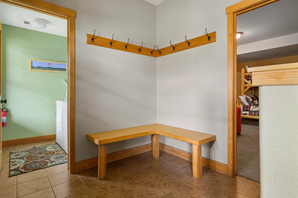 A functional mudroom featuring a wooden bench, coat hooks, and tile flooring. The space is designed for shedding boots, hanging coats, and storing gear after an outdoor adventure.