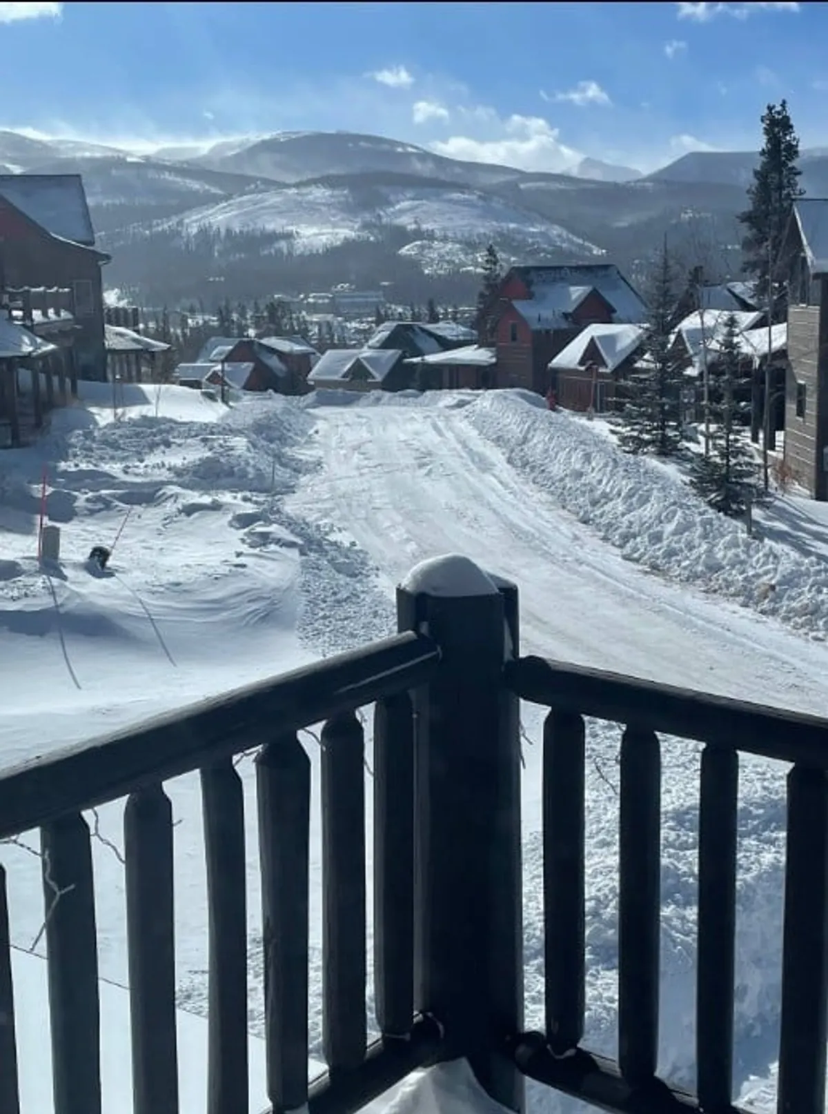 A wintery exterior shot highlighting a snow-covered road leading toward distant mountain views, bordered by charming houses nestled among the trees. The serene scene invites thoughts of cozy, exclusive mountain living with access to outdoor activities.